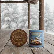 Two candles, one wooden and one with a blue label, on a wooden deck with a snowy landscape.